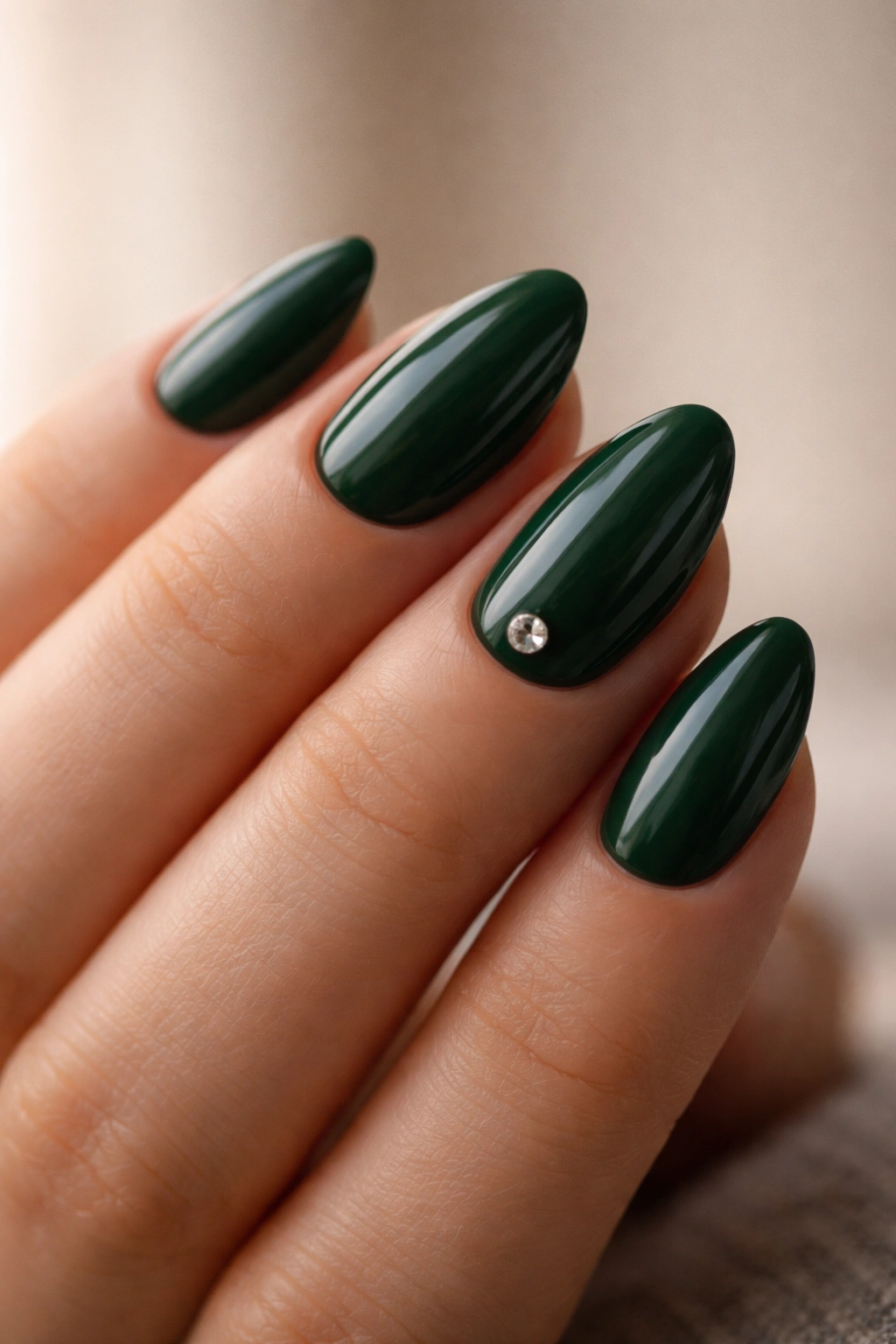 Close-up of deep green almond nails with a single accent gem near the cuticle