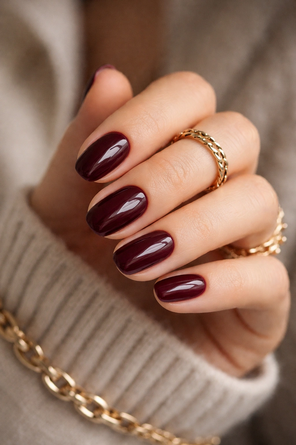 Deep maroon short oval nails on a hand with neutral background