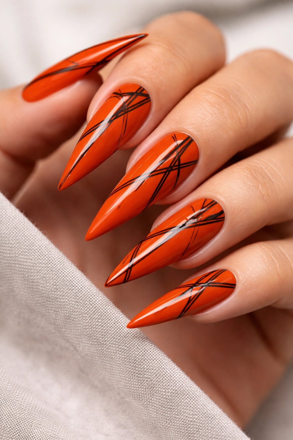 Close-up of deep orange nails with black geometric lines