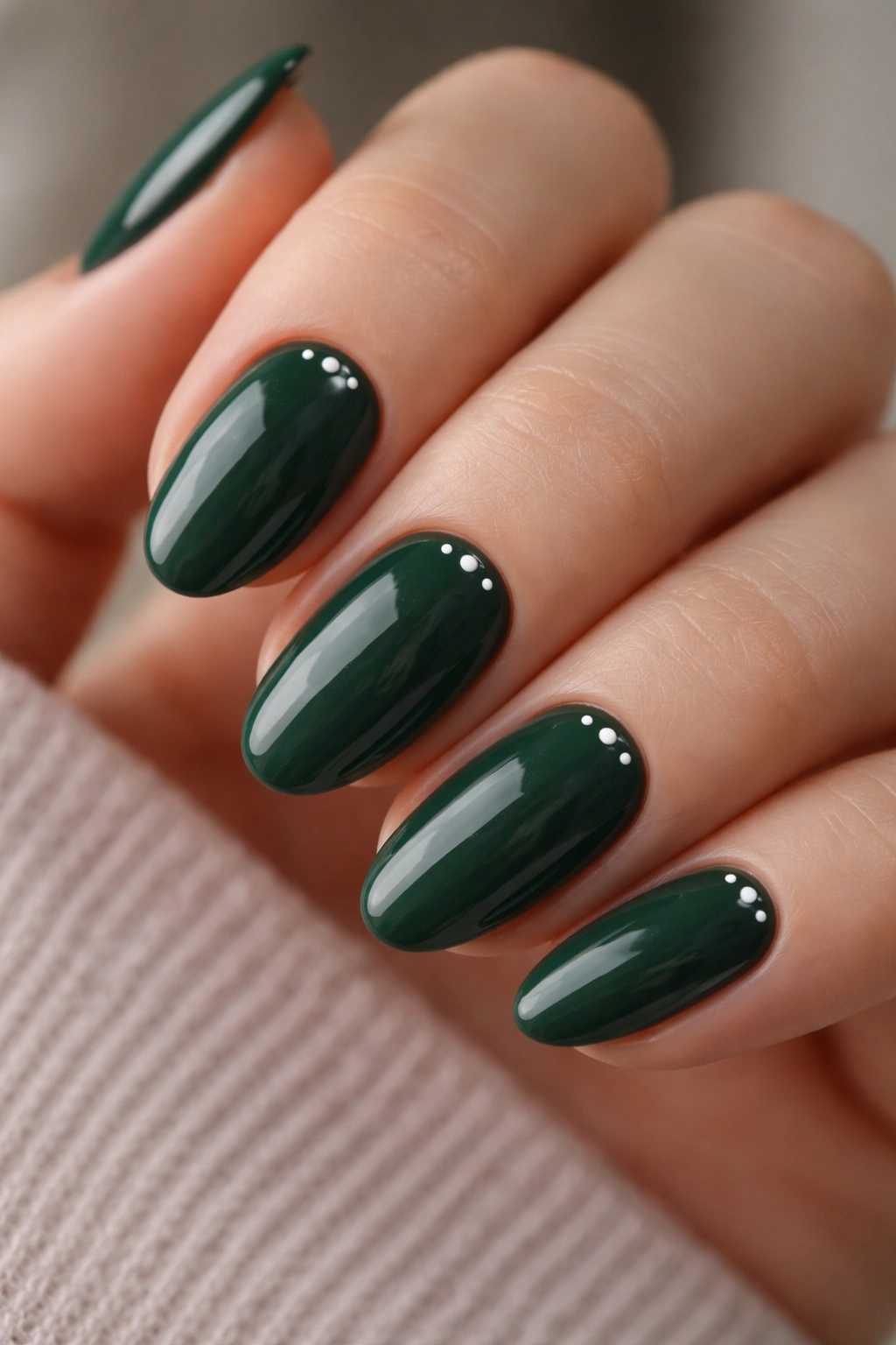 Close-up of short almond nails in deep pine green with tiny dot accents near the cuticle