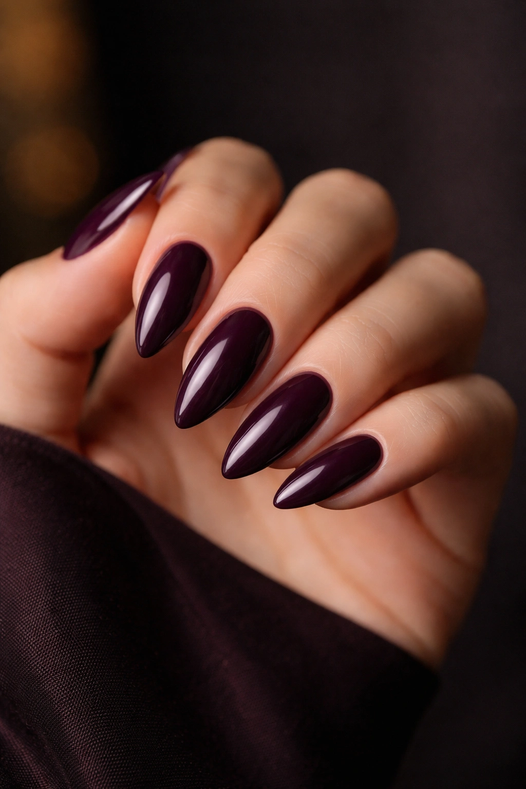 Deep plum almond nails with glossy finish on hand