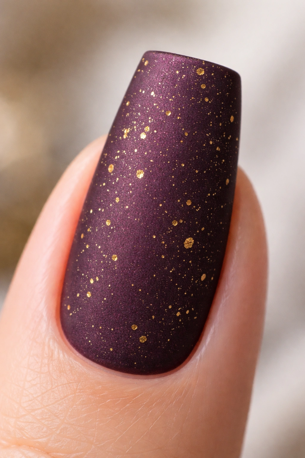 Close-up of deep plum coffin nail with gold flecks and matte finish