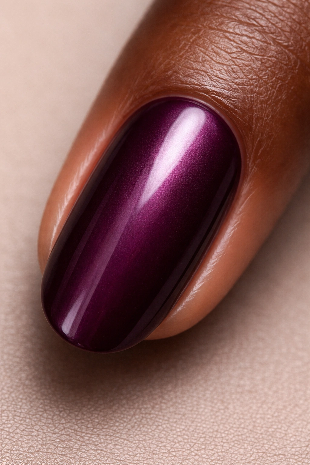 Close-up of a fingernail painted in deep plum satin finish