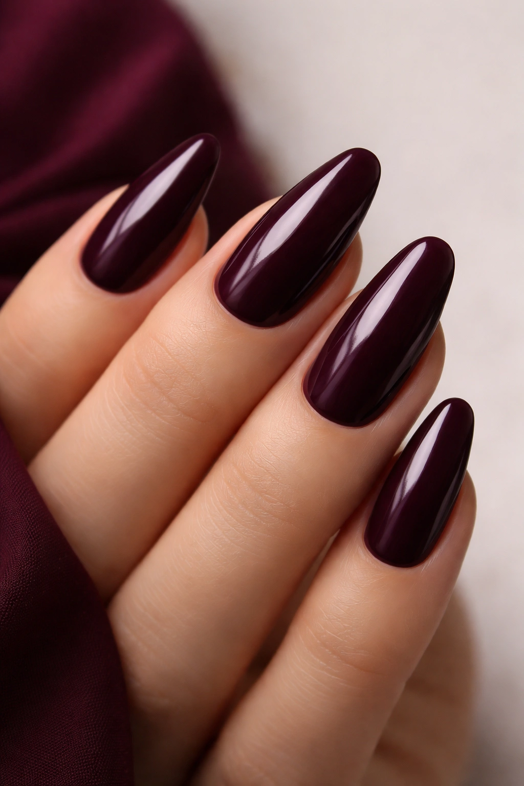 Close-up of deep plum nails on a hand with a neutral backdrop