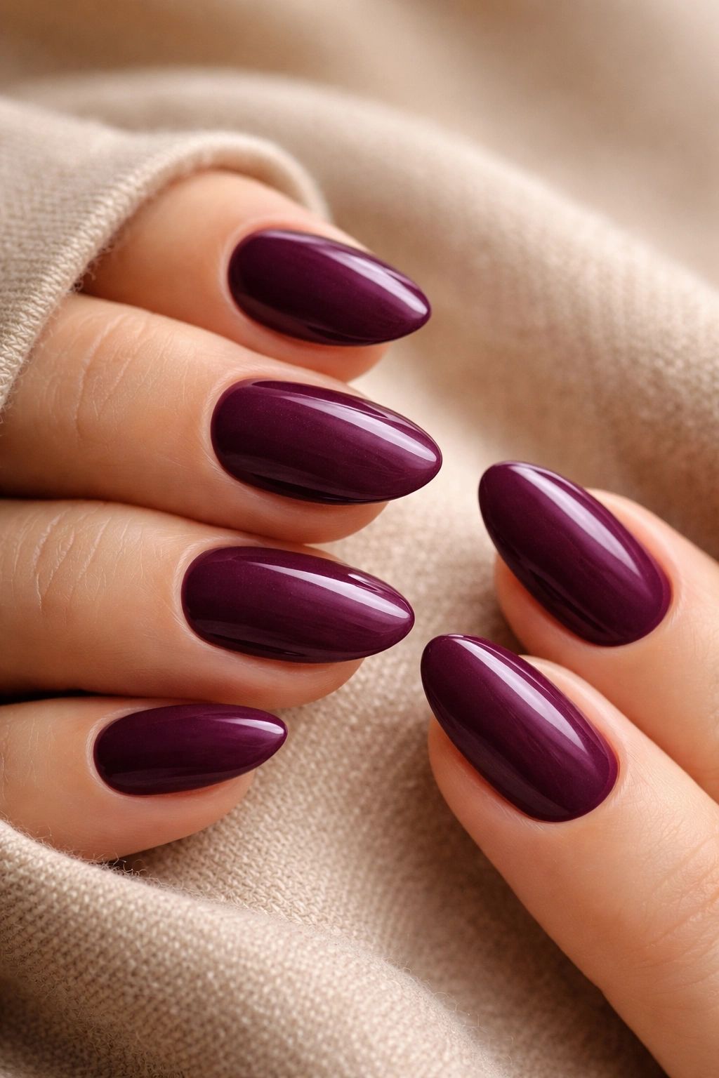 Close-up of short almond nails in deep plum with a cream finish