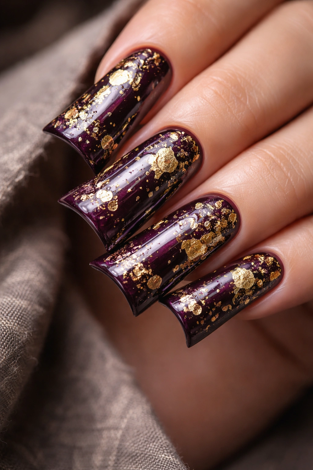 Duck nails in deep plum polish with gold foil accents.