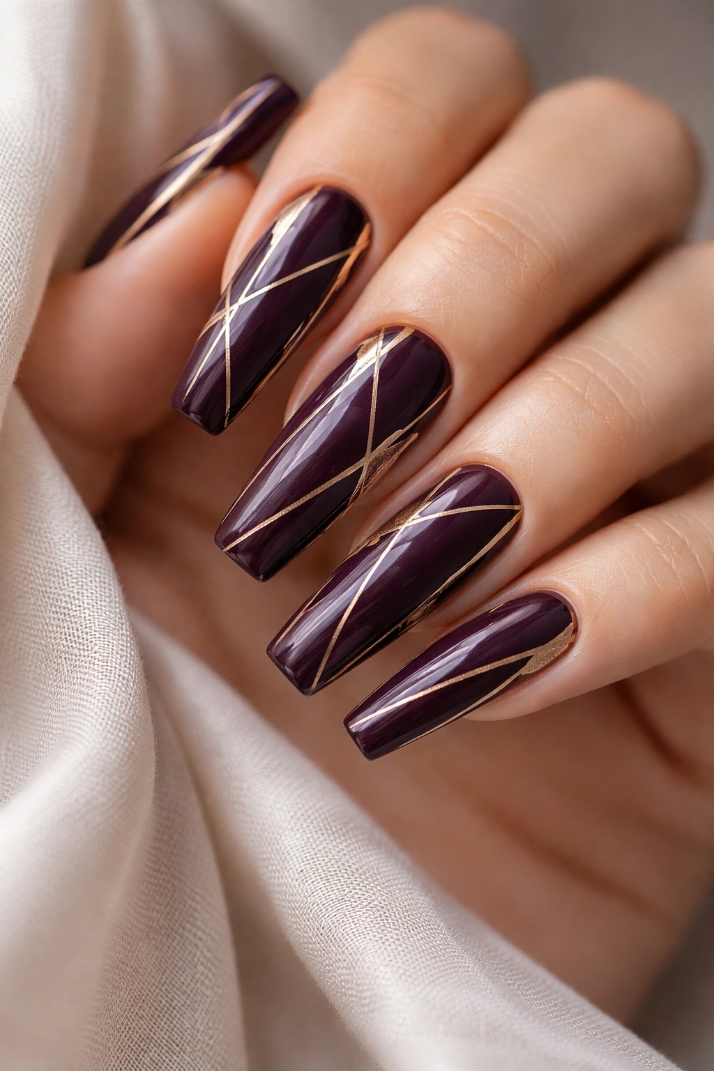 Close-up of coffin nails in deep plum with thin gold geometric lines