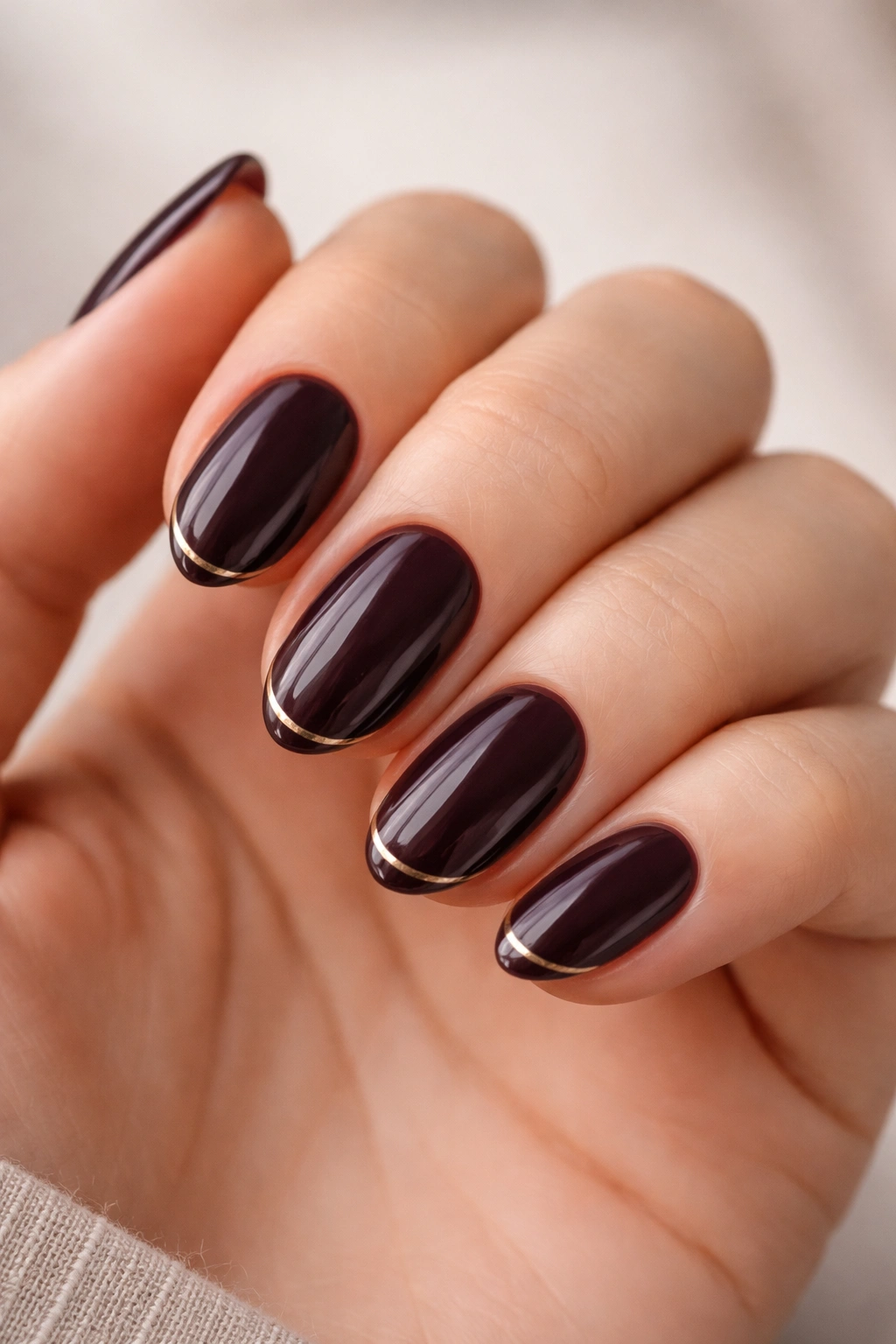 Close-up of short almond nails in deep plum with a tiny metallic line