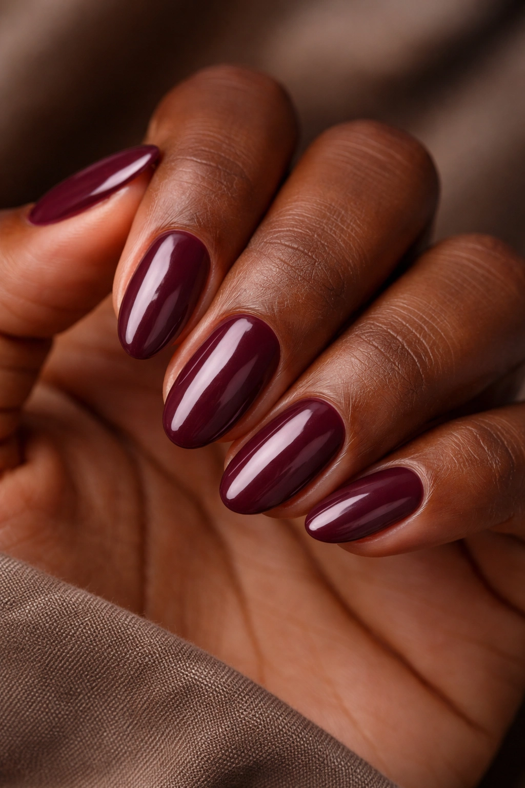 Close-up of deep plum short almond nails on dark skin