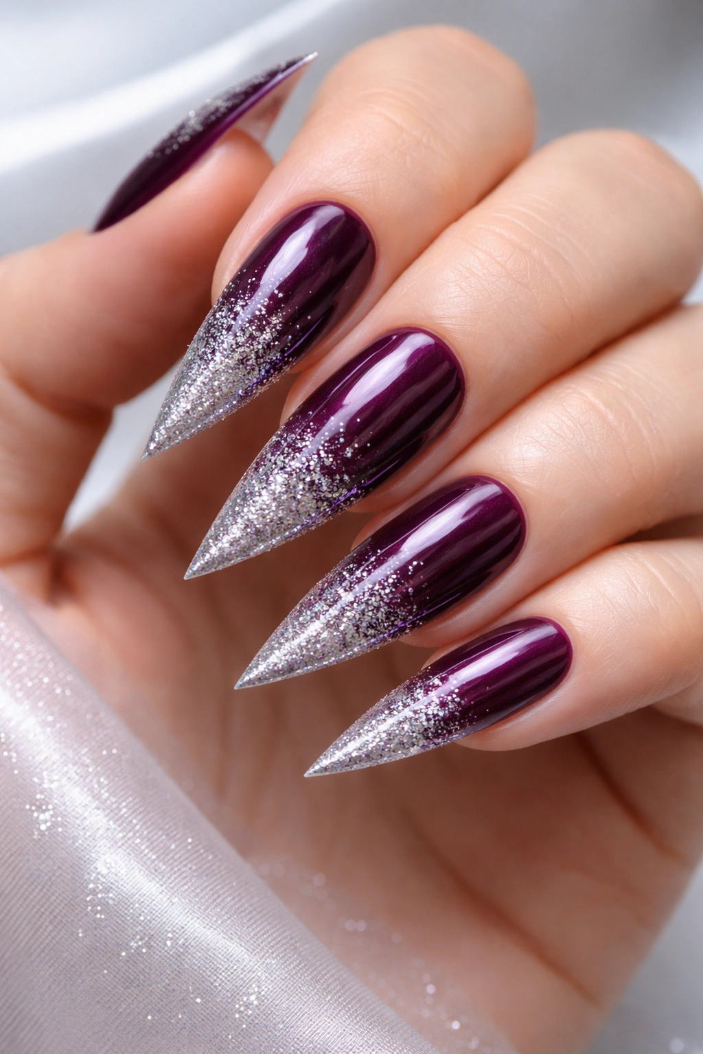 Close-up of deep plum stiletto nails with a silver sparkle gradient