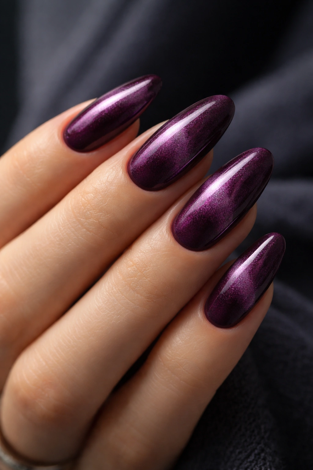 Close-up of long oval nails in deep plum with velvet finish and soft glow