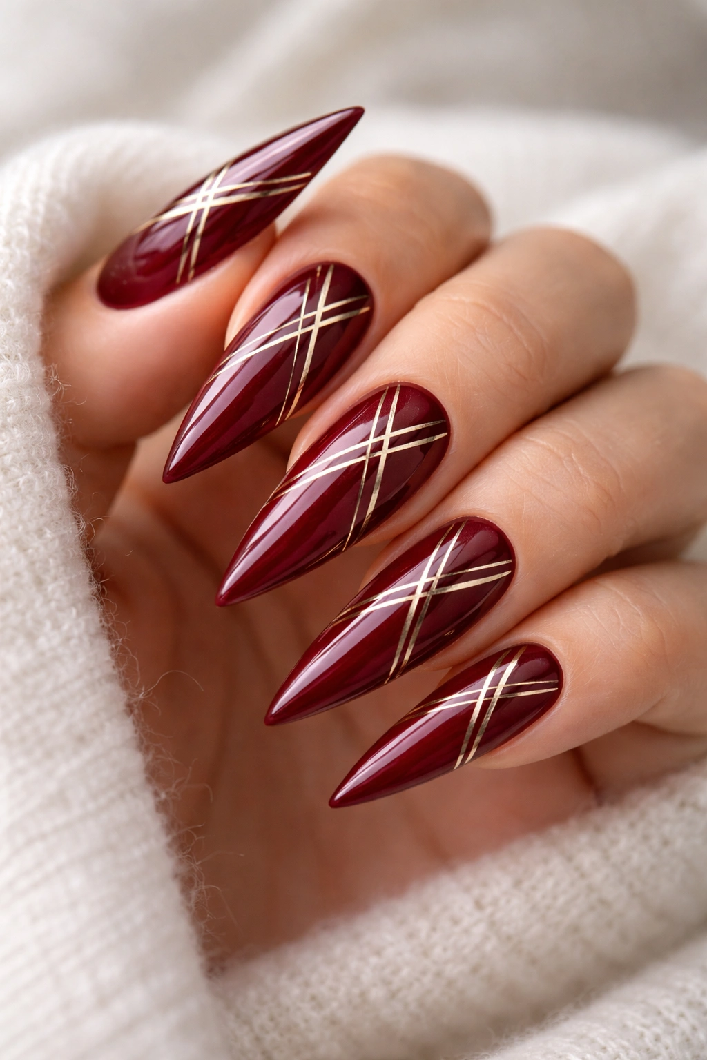 Close-up of deep red stiletto nails with gold geometric lines