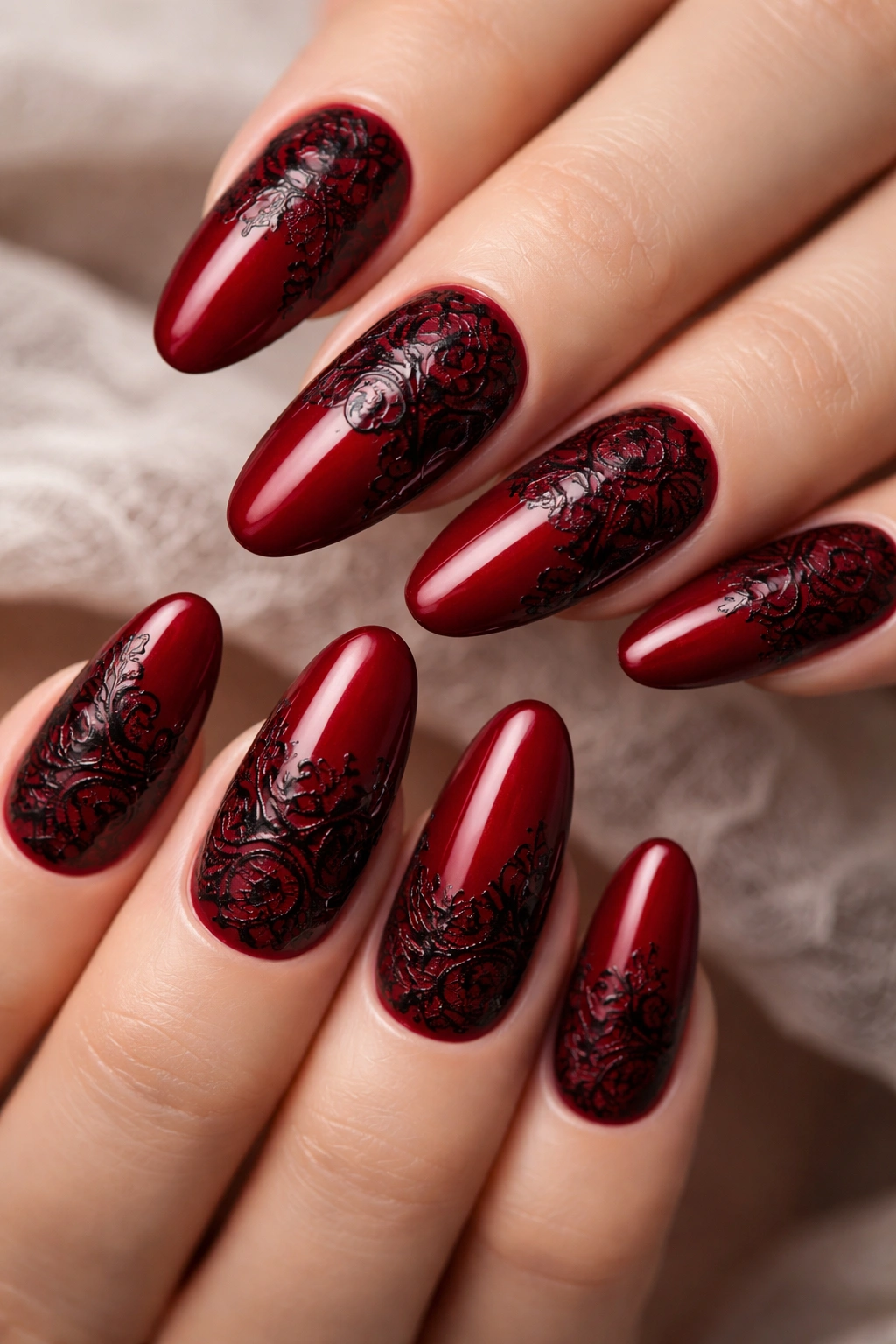 Close-up of long round nails with deep red color and black lace patterns