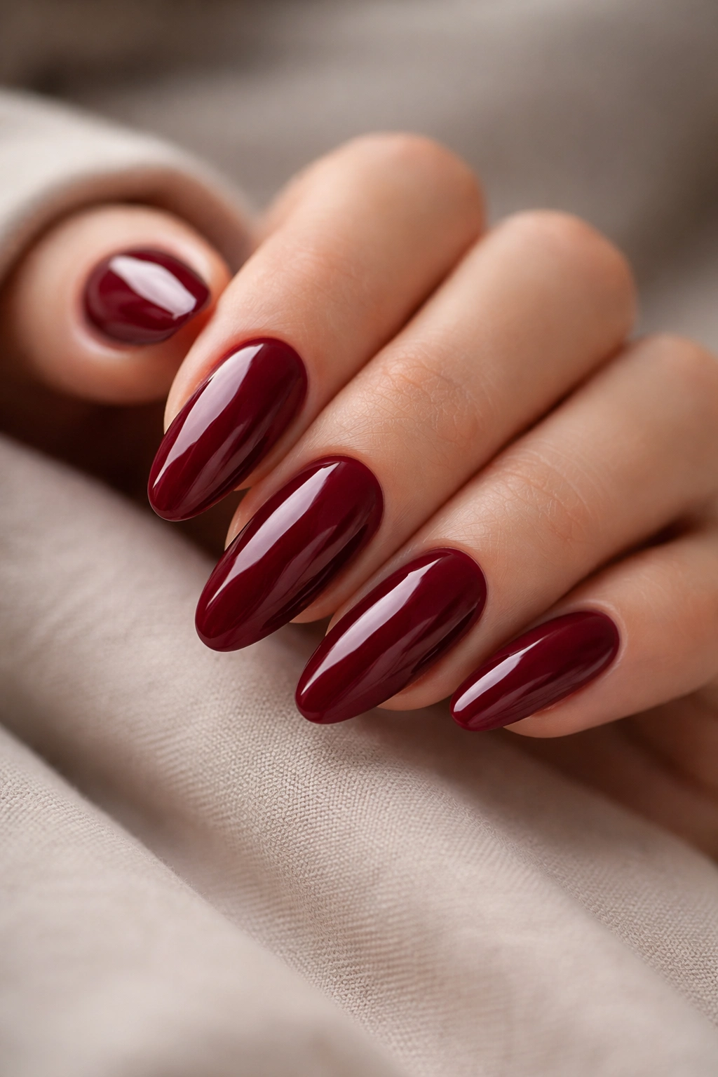 Close-up of long oval nails in deep red with almond-soft curve and glossy gel finish