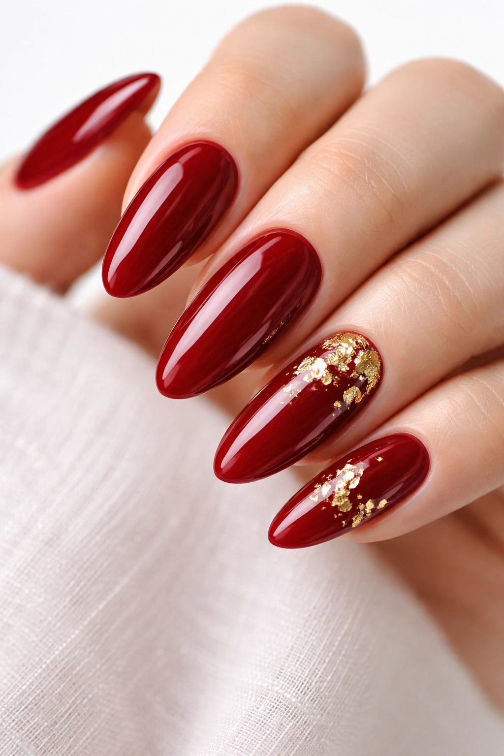 Close-up of long oval nails in deep red with gold leaf accents on a white background