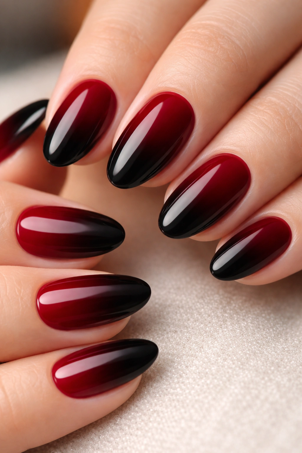 Close-up of short almond nails in a deep red to black ombre with glossy finish
