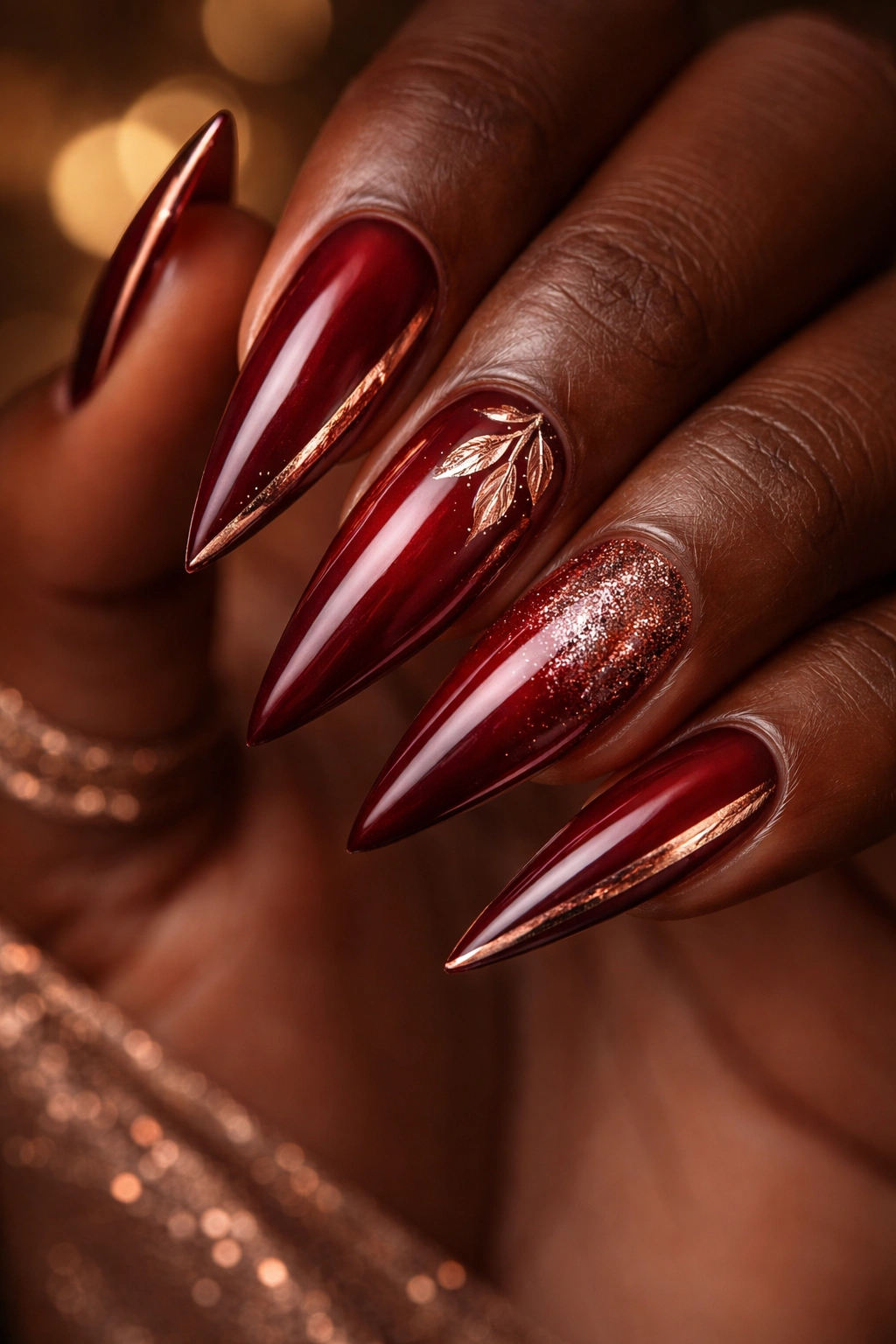 Deep red stiletto nails with rose gold accents showing warm metallic shimmer.