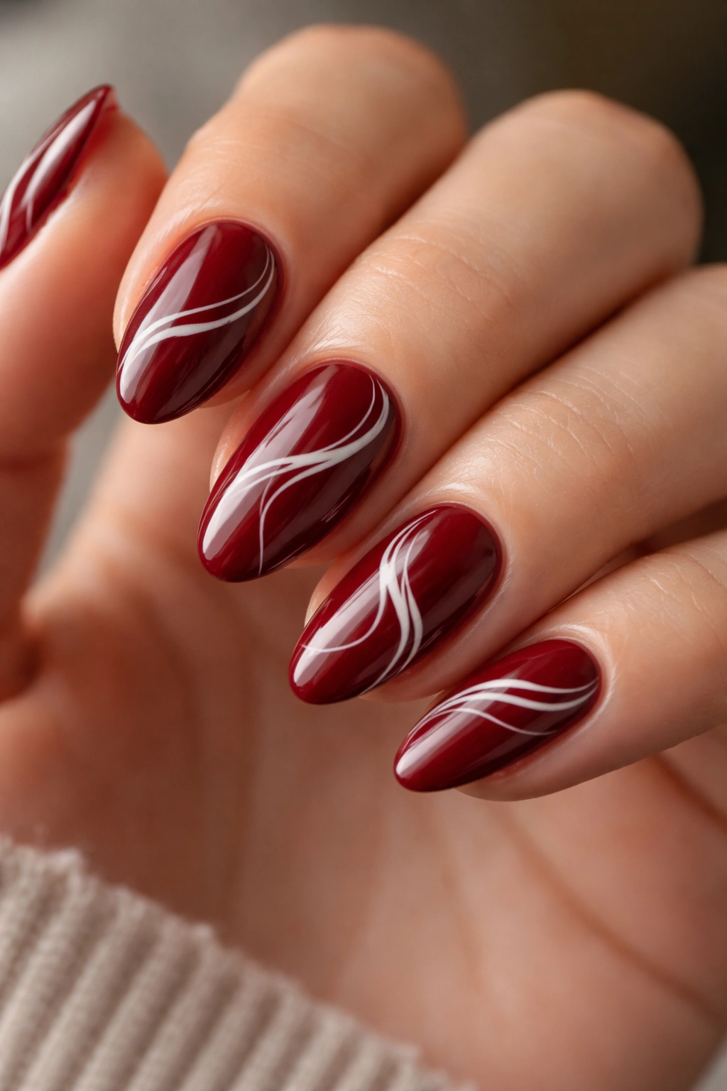 Deep red nails with white abstract swirls on short almond nails
