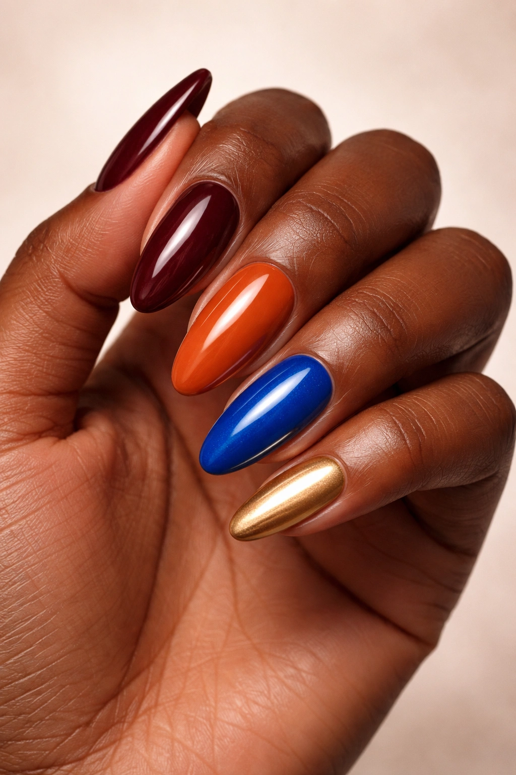 Deep skin hand with bold oxblood, orange, blue and gold nails