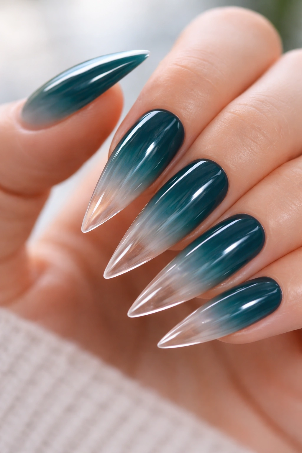 Close-up of deep teal to clear ombre stiletto nails fade-to-nothing