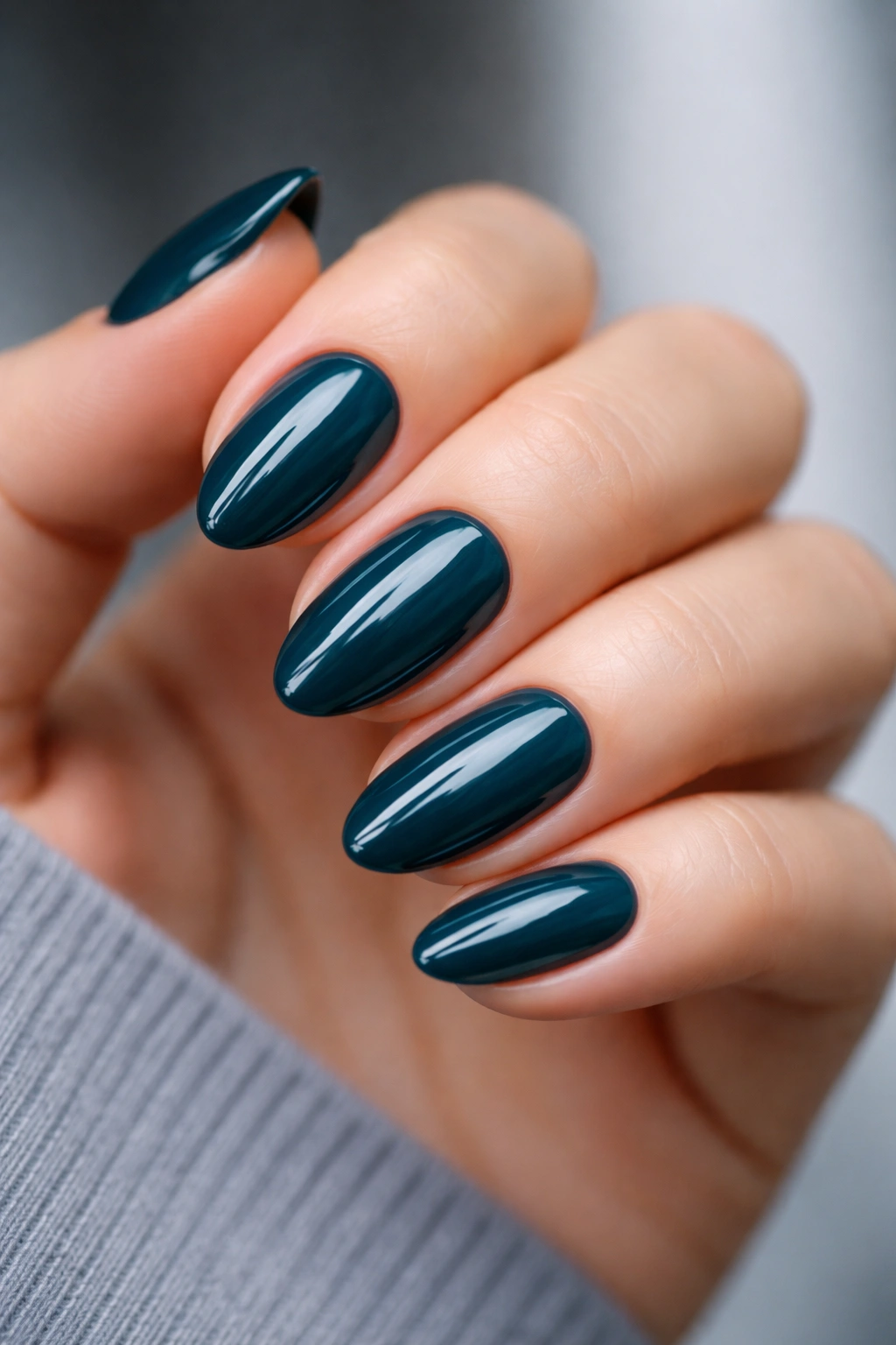 Close-up of short almond nails painted in deep teal glass finish against a neutral background