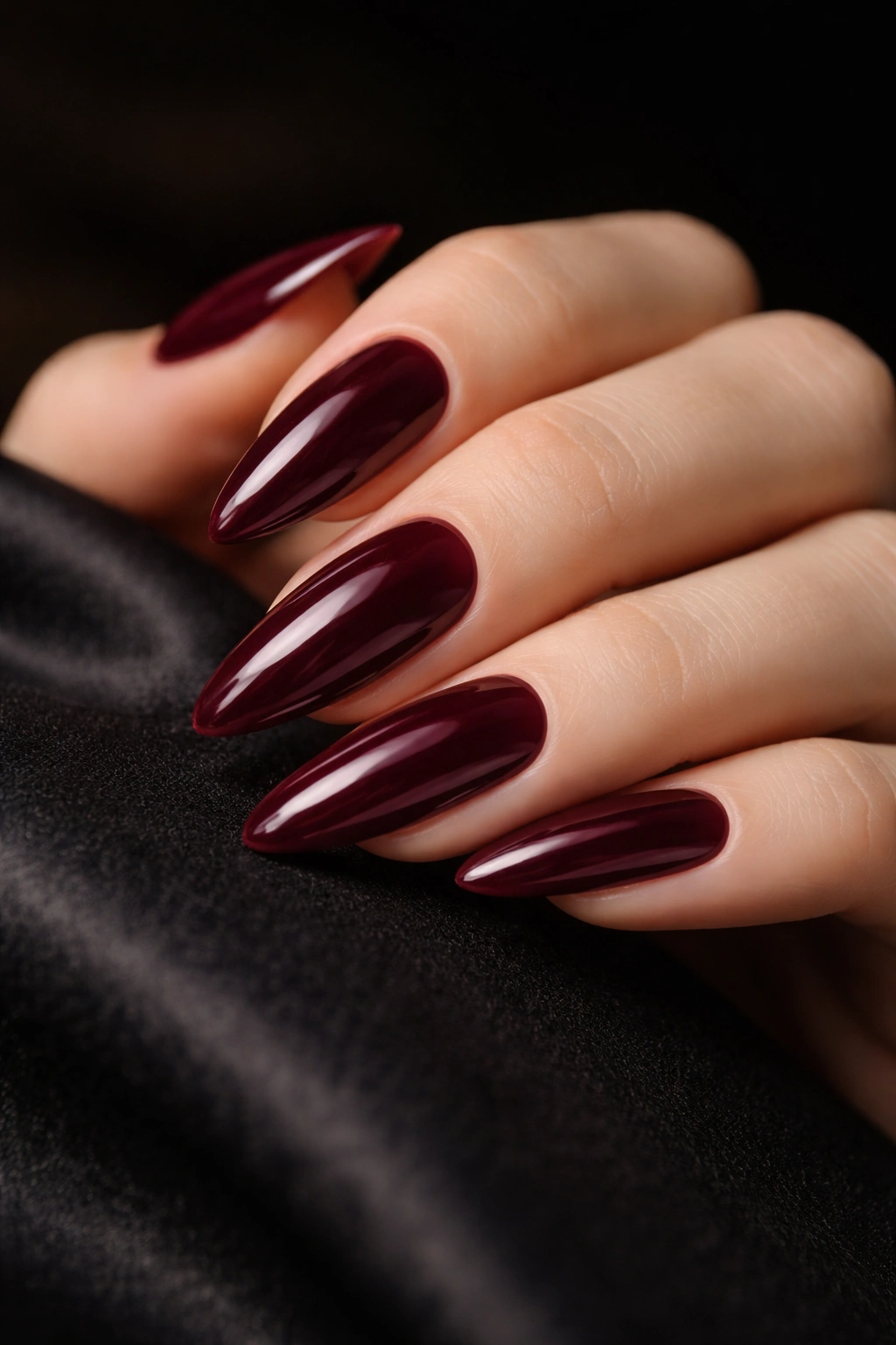 Close-up of deep wine almond nails with glossy finish on a hand