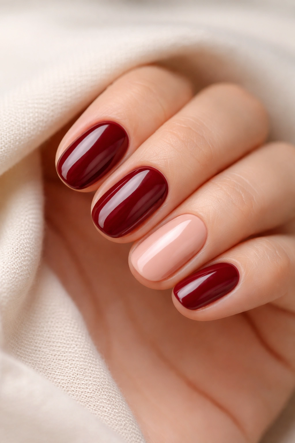 Close-up of four deep wine nails with one nude accent on a short oval hand.