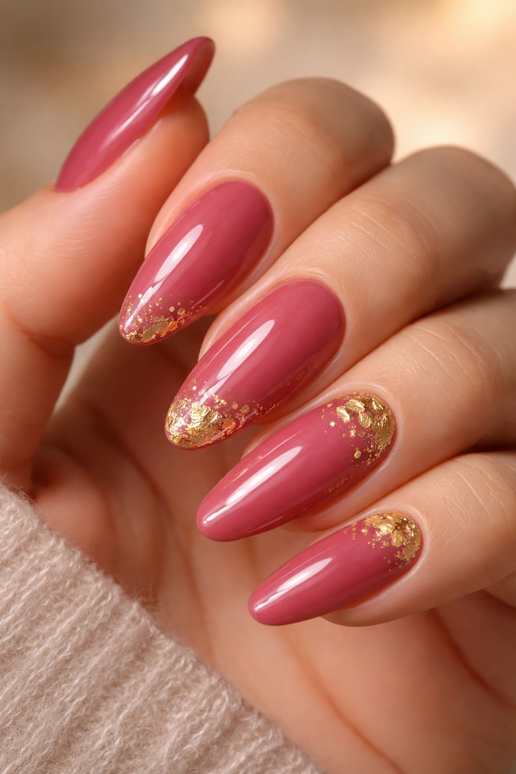 Long oval nails in deep rose pink with gold leaf accents.