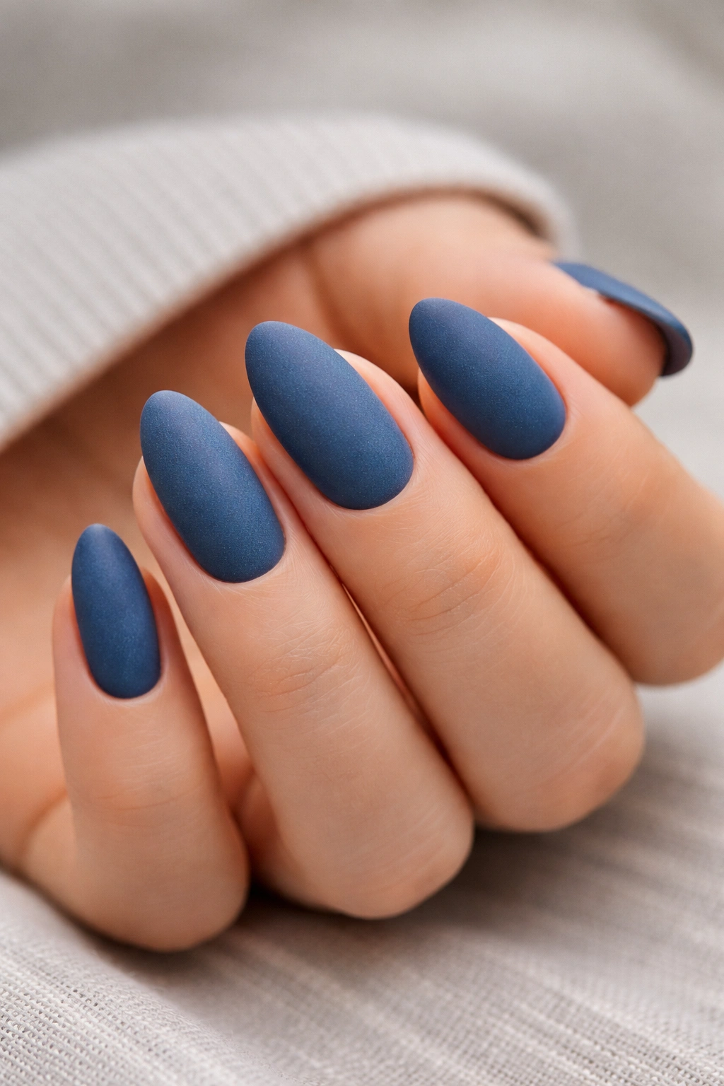 Close-up of short almond nails in denim blue matte with fabric-like texture.