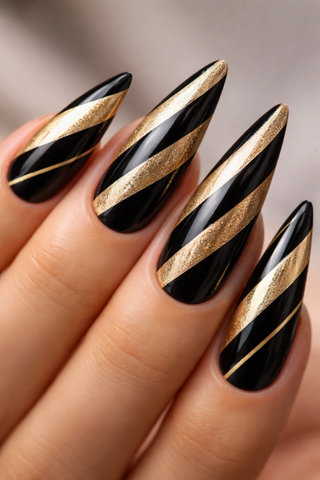 Close-up of stiletto nails with diagonal black and gold stripes.