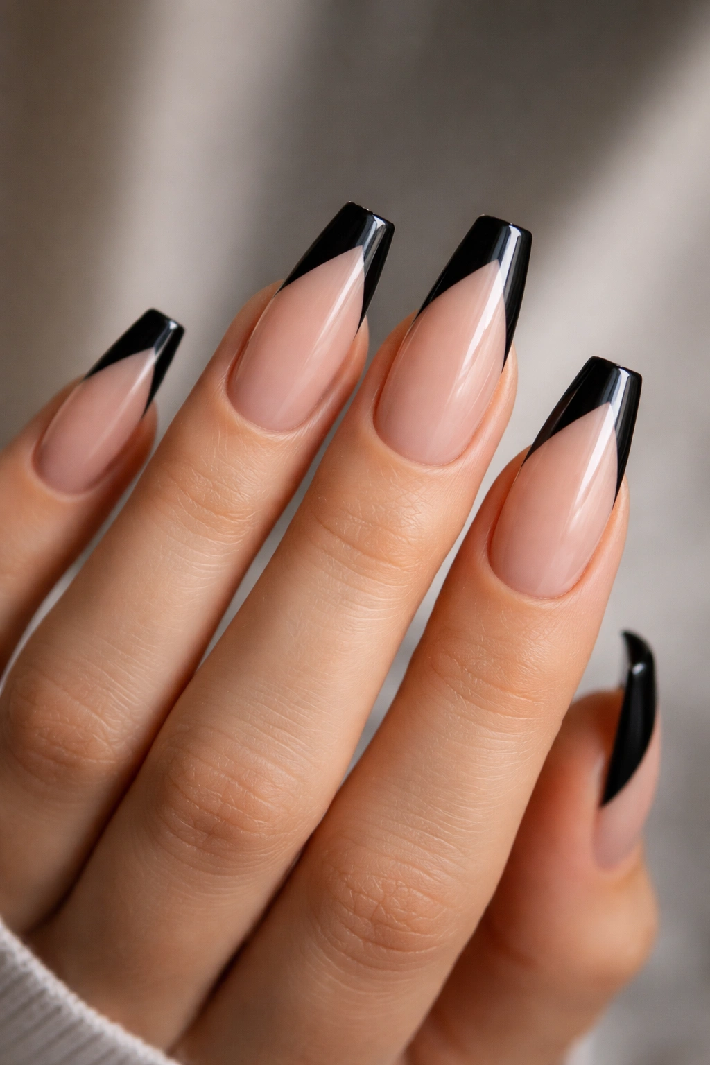 Close-up of a hand showing diagonal side-swept black tip ballerina nails on nude base