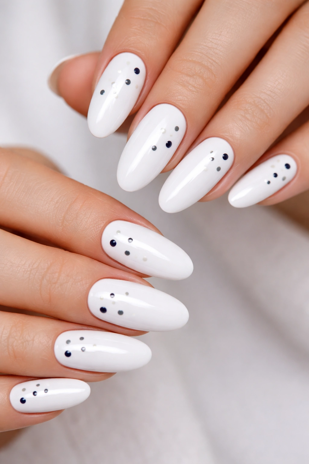 Close-up of white long oval nails with simple dot details in navy and gray