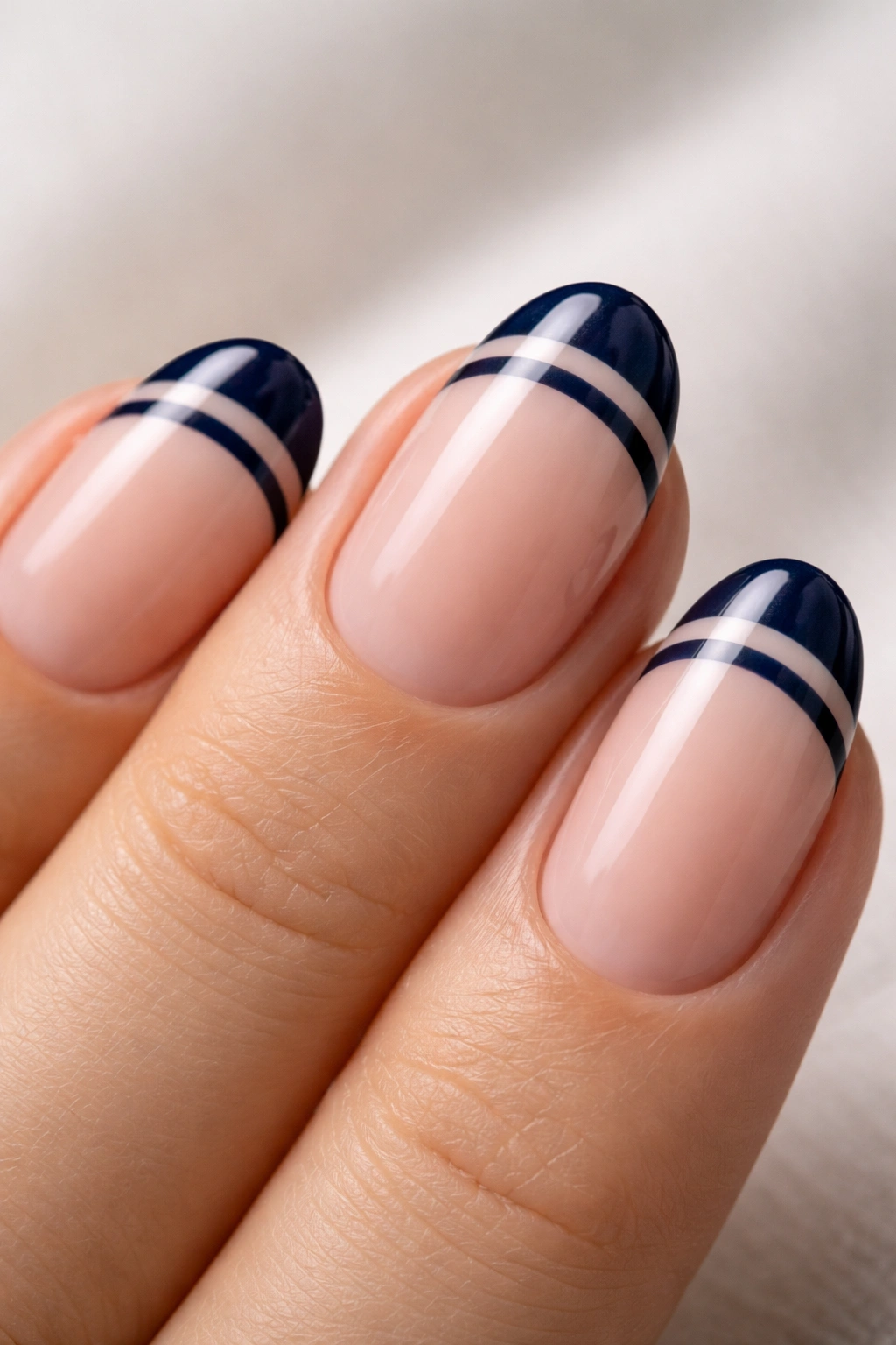 Close-up of a short almond nail with two navy stripes at the tip and a nude gap
