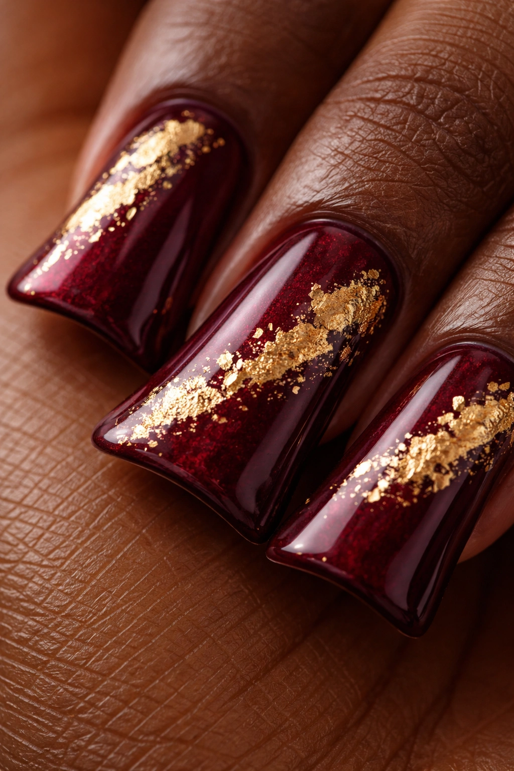 Close-up of duck nail tip in deep burgundy with gold leaf accents on a neutral background