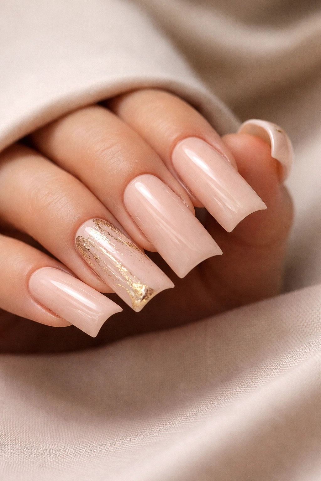 Close-up of duck nails on a hand with soft nude base and gold accents