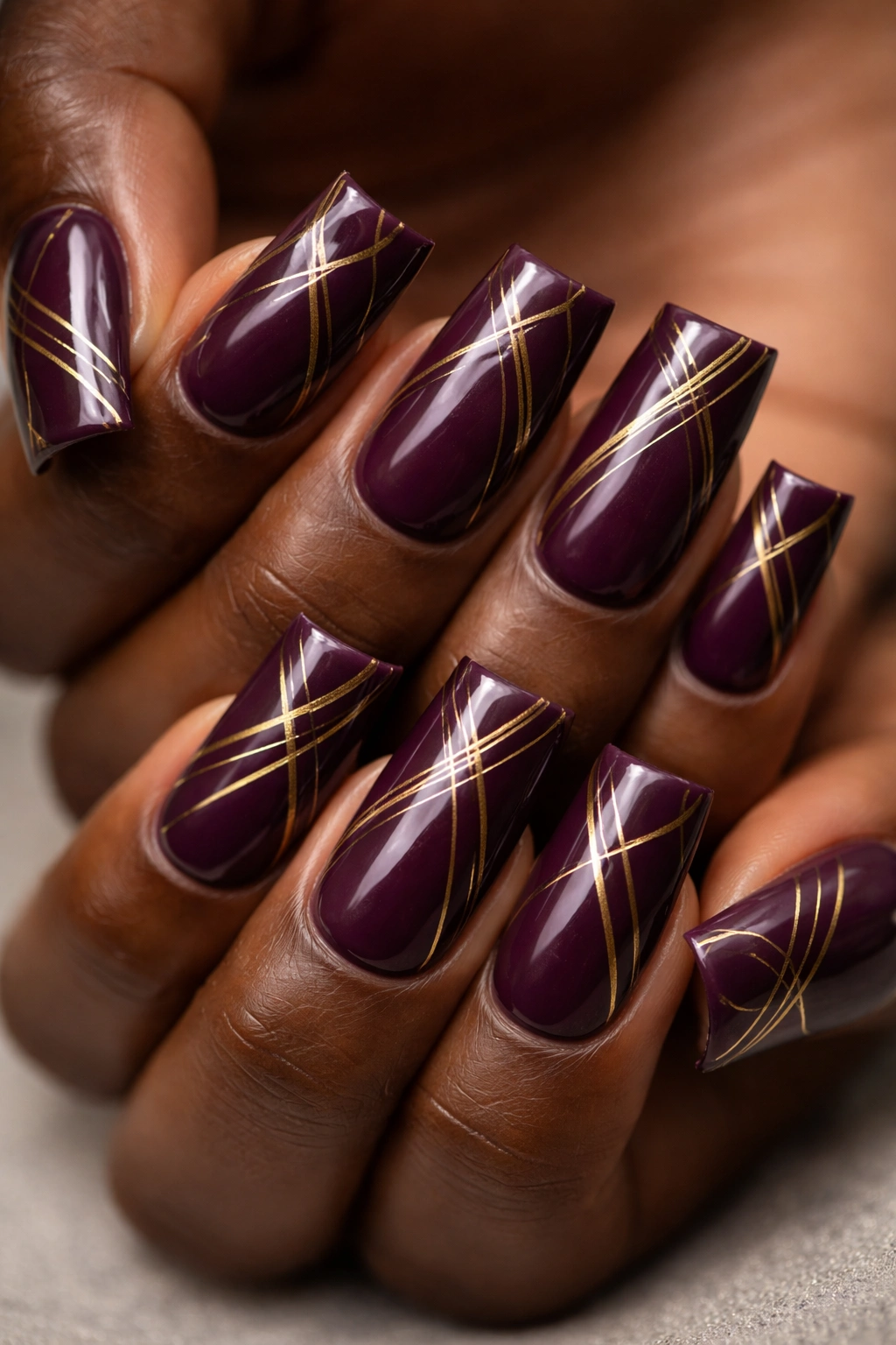 Close-up of duck nails with deep plum base and gold geometric lines on dark skin