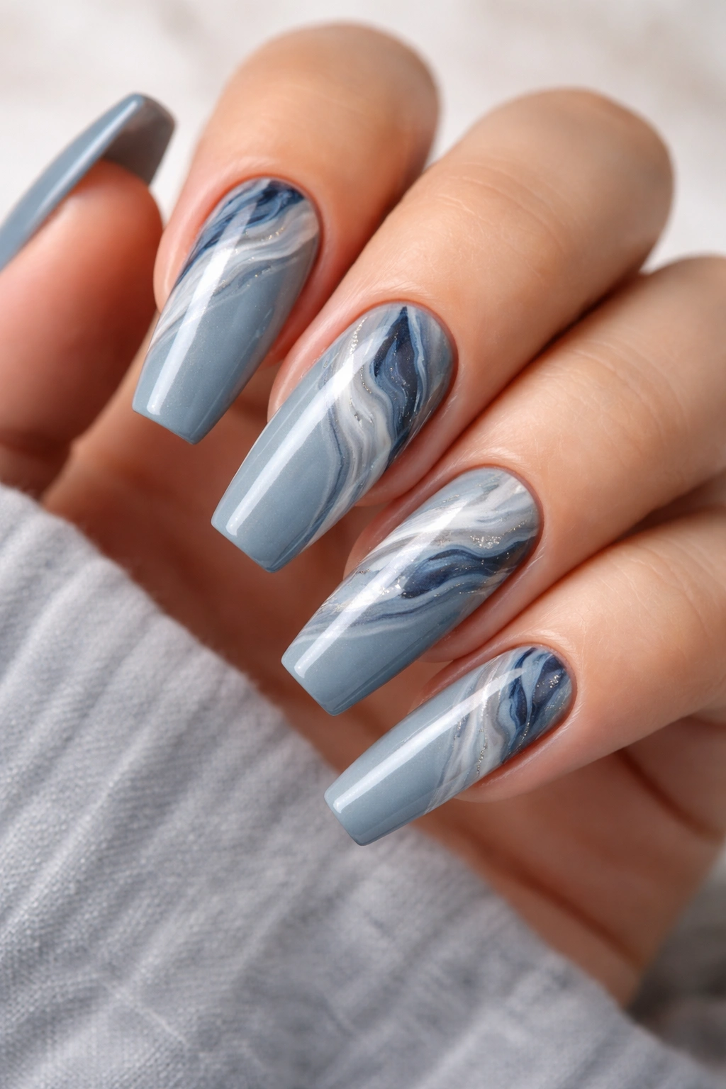 Close-up coffin nails in dusty blue with white gray navy marble swirl, glossy finish.