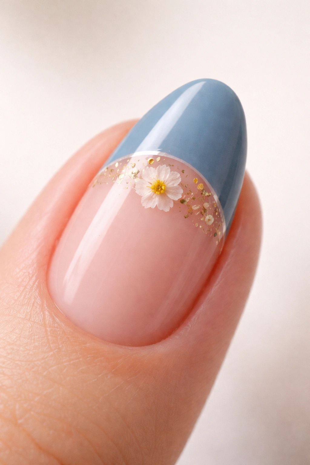 Close-up of a short almond nail with dusty blue French tip and pressed flower accent at the boundary.