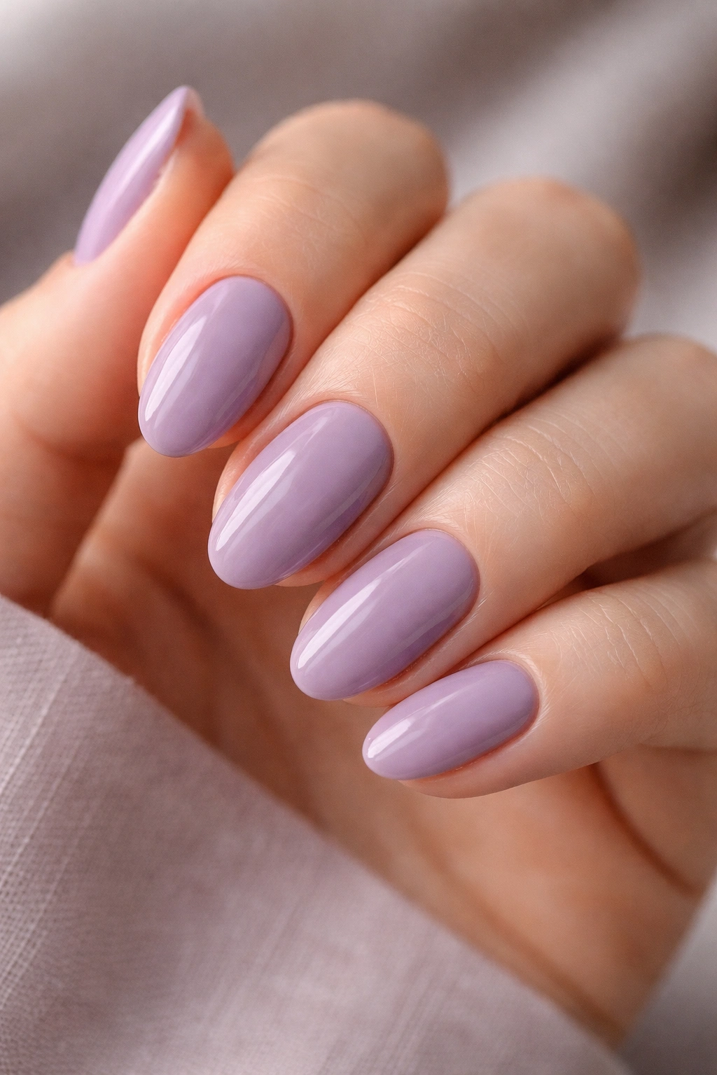 Close-up of short almond nails painted dusty lavender with a glossy finish