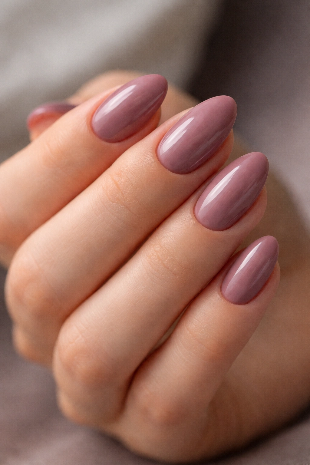 Close-up of short almond nails painted dusty mauve on a neutral hand