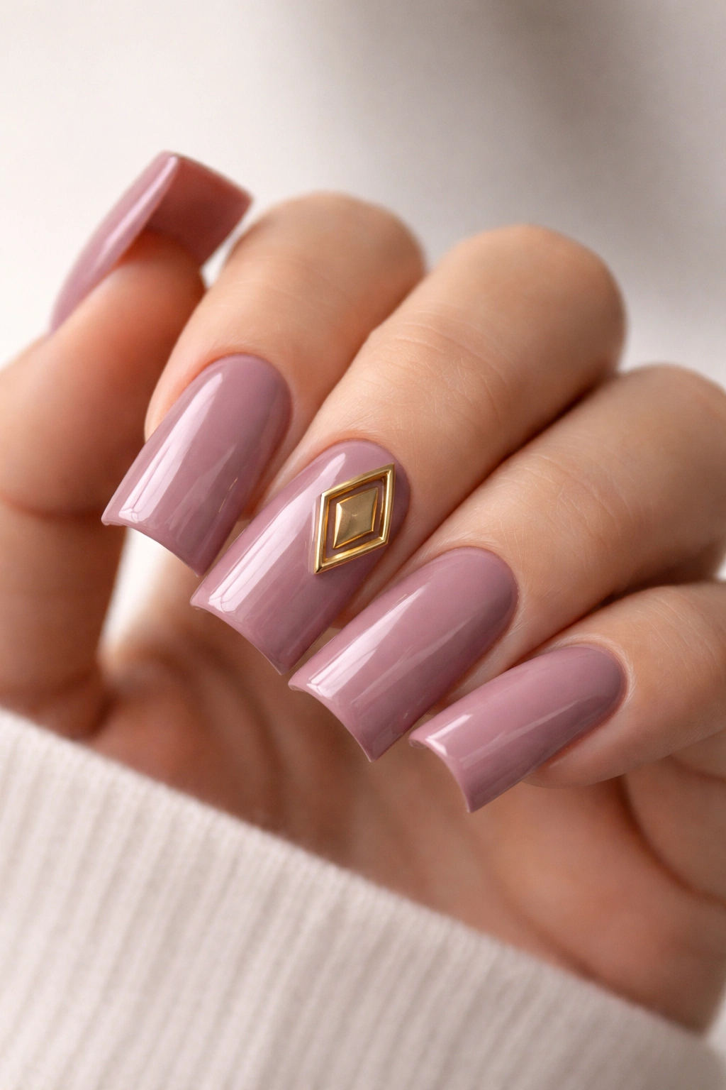 Dusty mauve-pink nails featuring a gold geometric charm on one nail