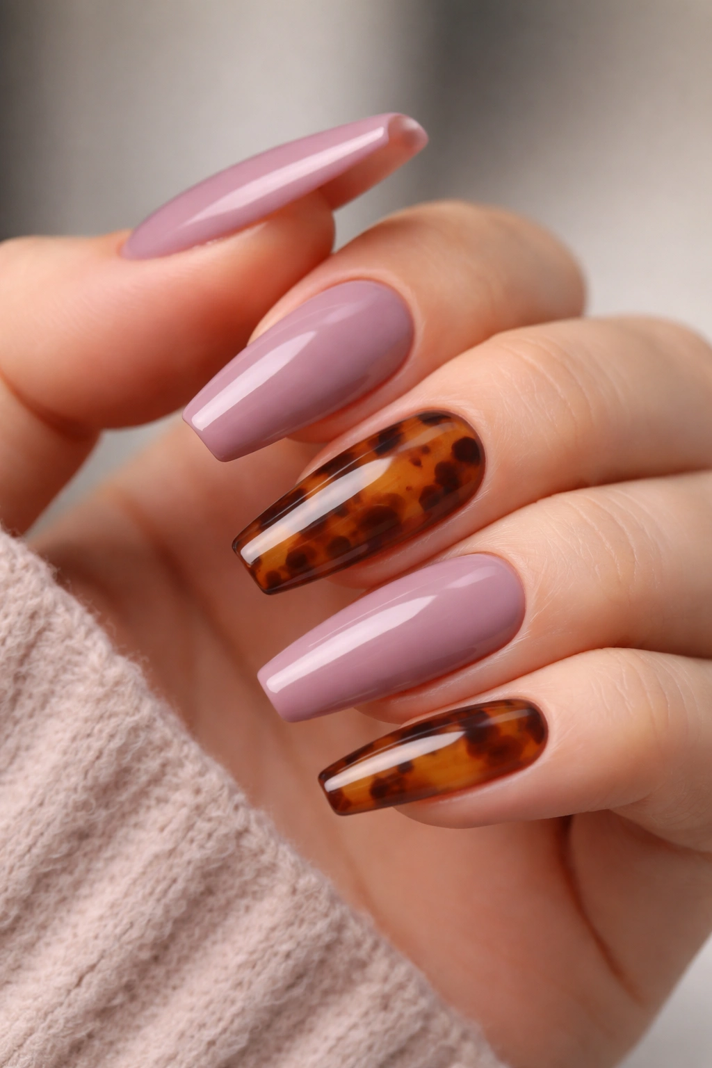 Close-up of dusty mauve nails with a tortoiseshell accent on one or two nails, glossy finish.