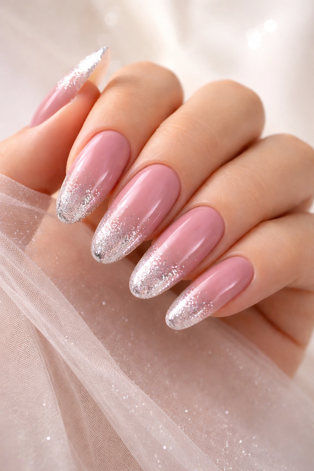 Nails with dusty rose base and silver glitter tips in a soft ombre on long round nails