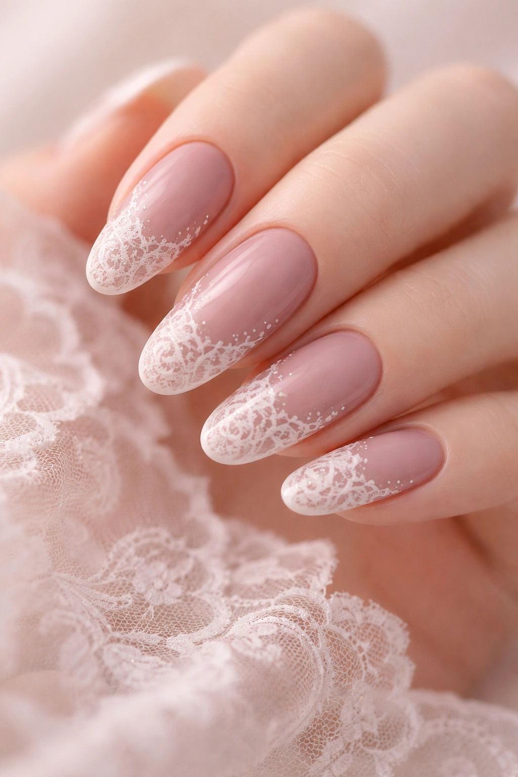 Close-up of dusty rose nails with delicate white lace patterns on long oval nails