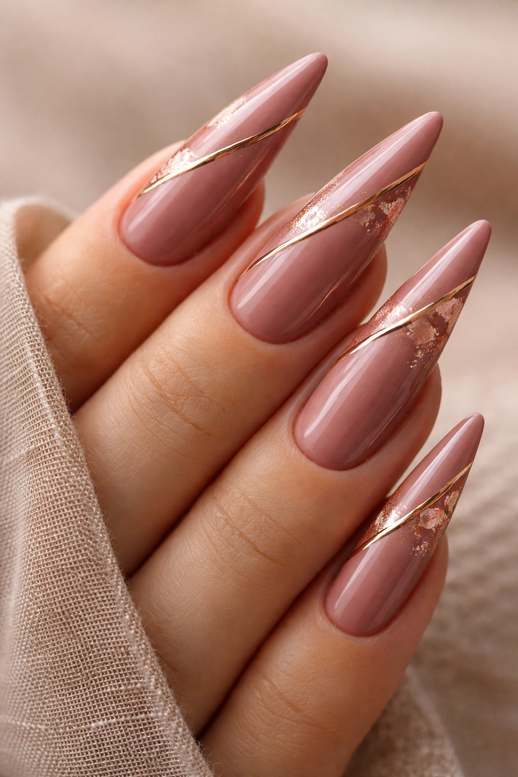 Dusty rose stiletto nails with gold metallic lines on a neutral backdrop
