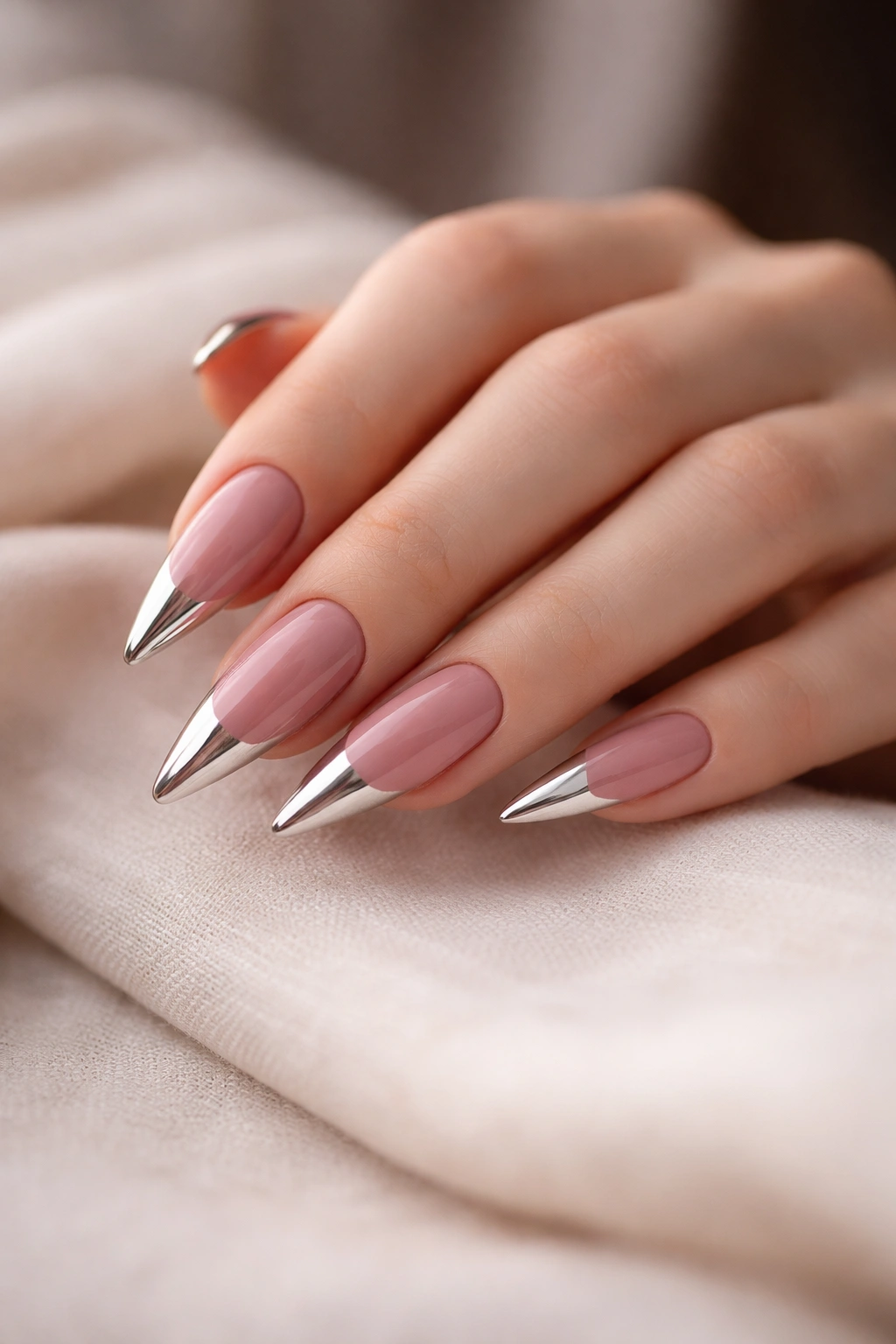 Close-up of dusty rose stiletto nails with metallic tips on a hand