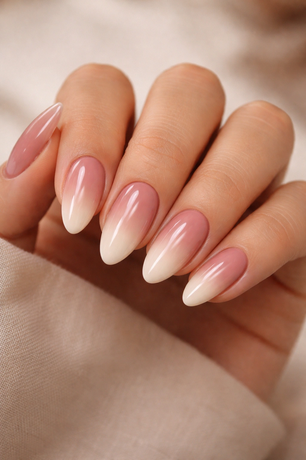 Close-up of almond nails with dusty rose to cream ombre in warm studio lighting