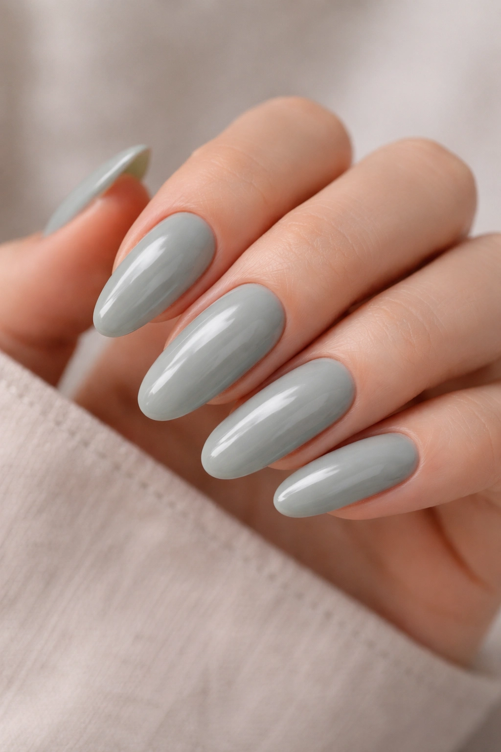 Close-up of a long oval nail painted dusty sage gray with a creamy milky base