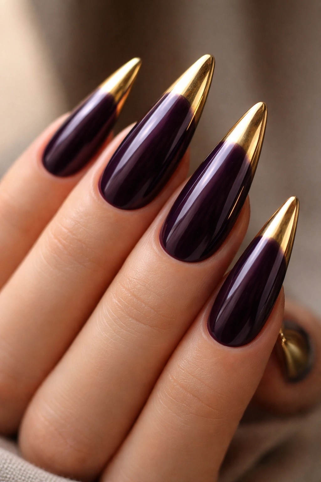 Close-up of eggplant nails with metallic gold tips on stiletto nails
