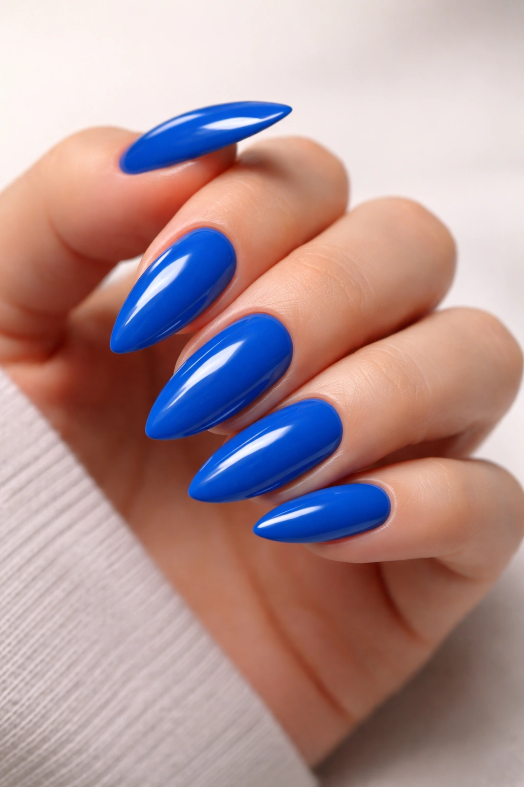 Close-up of electric blue almond nails with a high-gloss finish on a hand